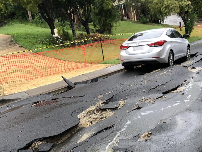 Suburban road damaged by floodwater with grounded car in road